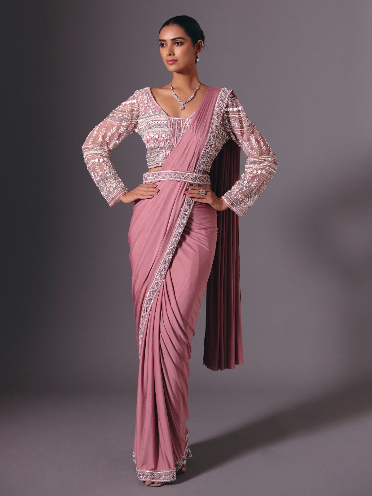 This onion pink lycra saree dazzles with intricate cutdana, sequin, bead, diamond and pearl work. Styled with a chic designer waist belt, it offers a graceful, modern silhouette. Ideal for wedding celebrations, receptions and glamorous parties.